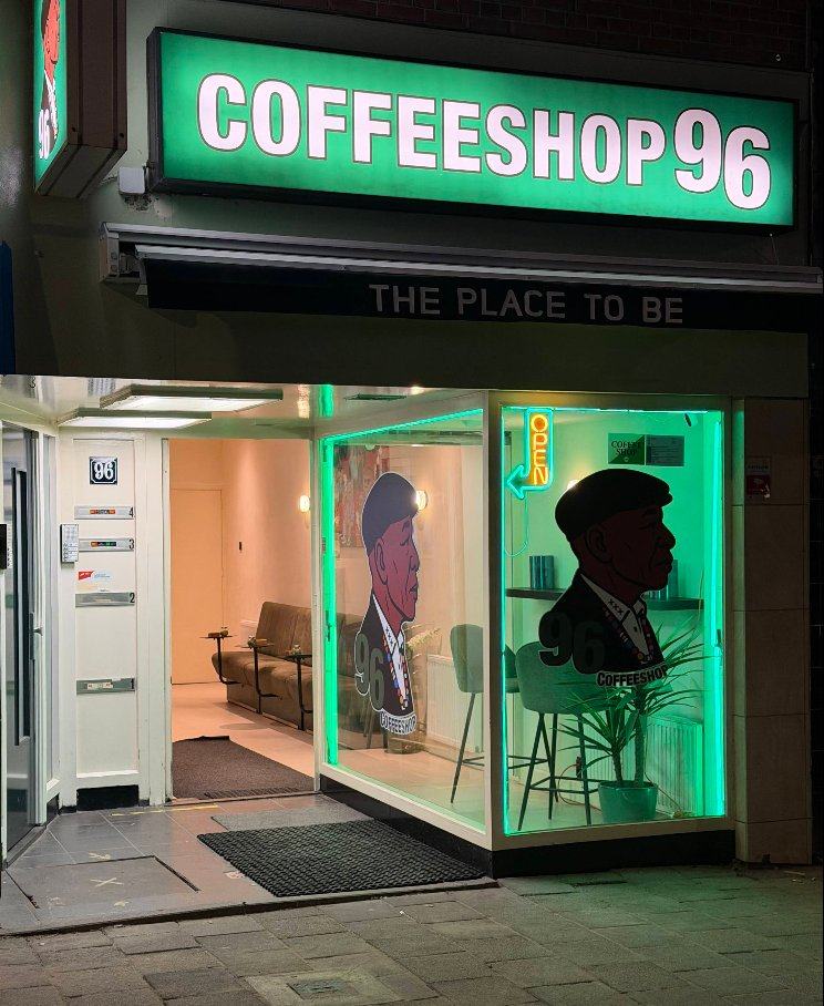 Coffeeshop 96 at night — the green-lit sign and gentleman silhouettes glowing through the windows